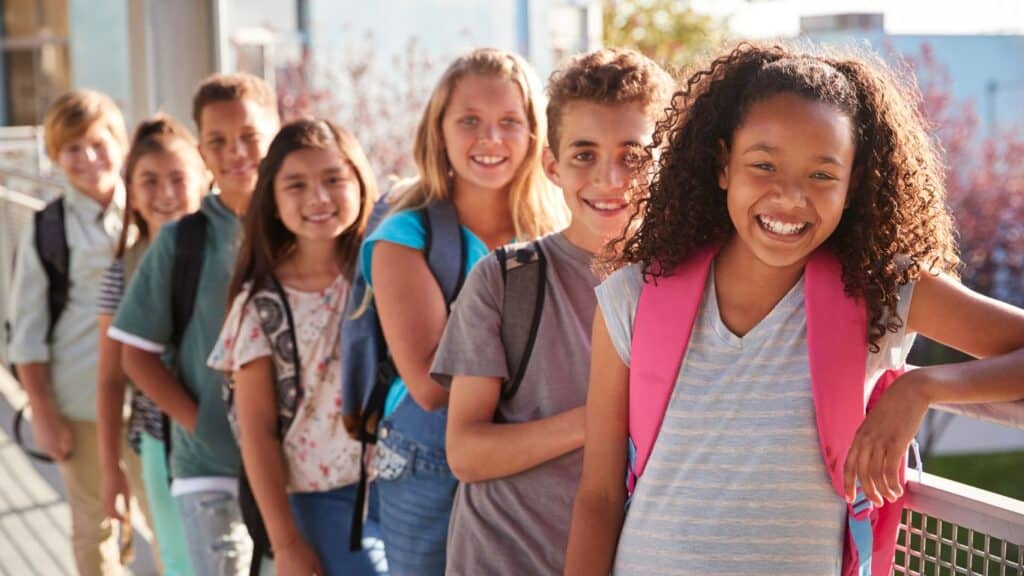 A group of school kids with backpacks, smiling.