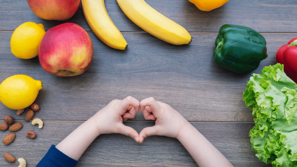 Various fruits and vegetables surrounding a child's hands forming a heart shape.