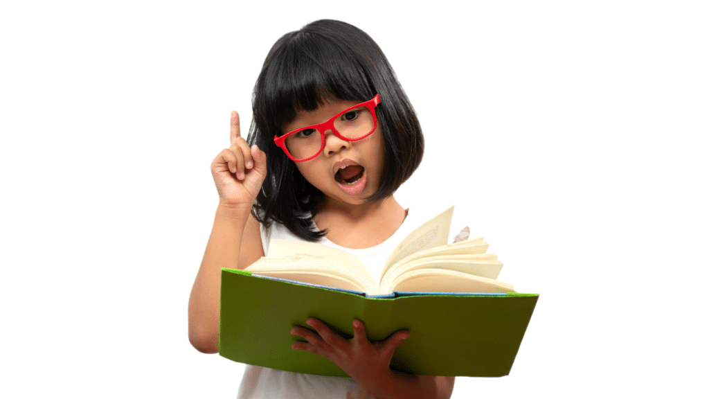 A little girl with short black hair and red glasses is holding a green book. The book is open, and she's rasising her right hand.