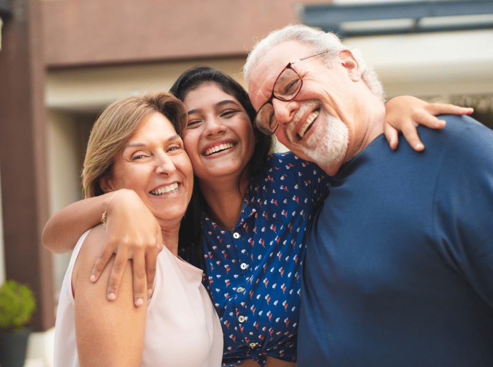 A smiling teenager with her grandparents. Her arms are around the two grandparents.