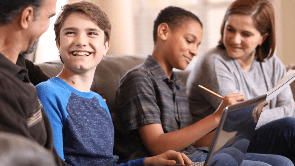 Two male tweens and two adults are sitting on a couch. The adults appear to be helping the tweens with their homework.