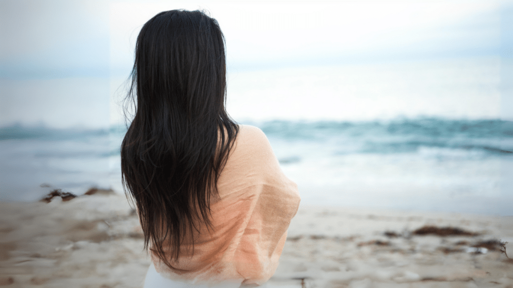 The back of a woman with black hair looking at the ocean.