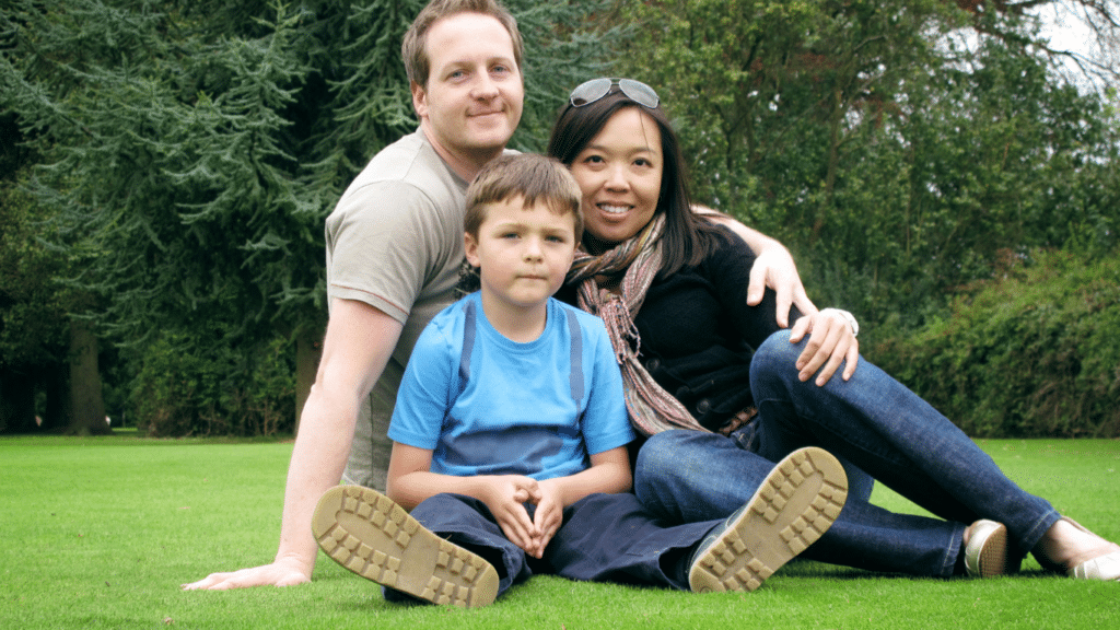 A toddler boy sitting with his parents, enjoying a day at the park.