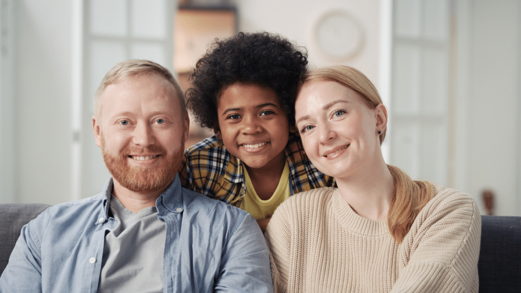 A diverse and happy family portrait with two white parents and a smiling black child.