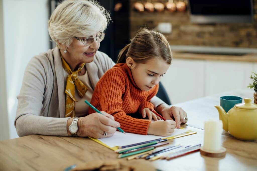 A grandmother and granddaughter drawing together at a table.
