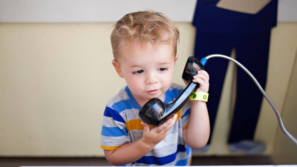 A young blond boy holding a classic black phone handset.