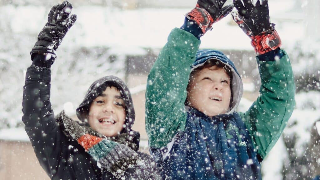 Two young boys happily playing in the snow and smiling.