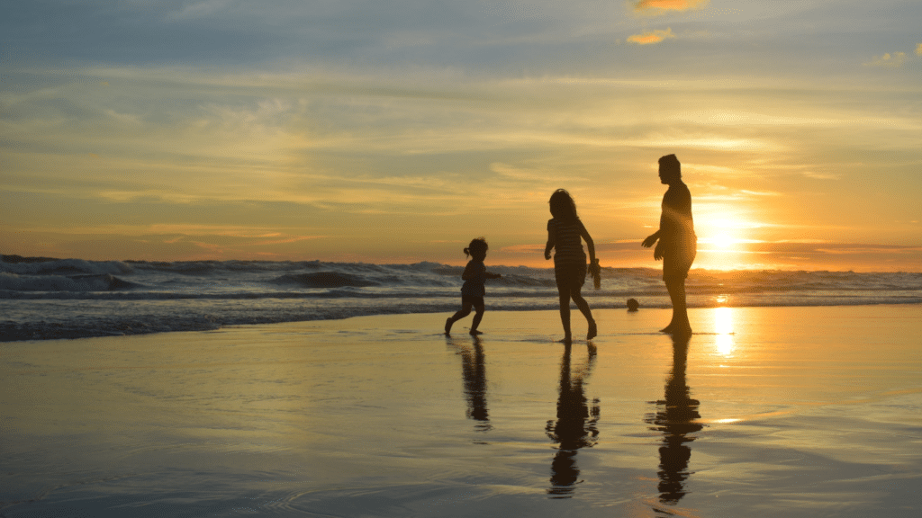 Family of three enjoying the beach at sunset.