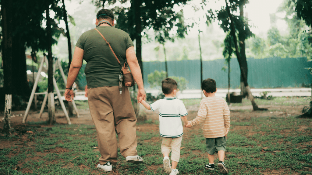 Two little boys and their dad holding hands in the park.