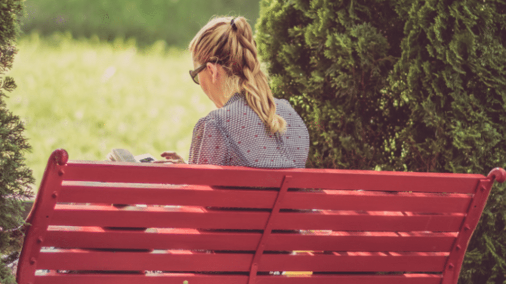 Back view of a woman on a bench with a book in hand, waiting.