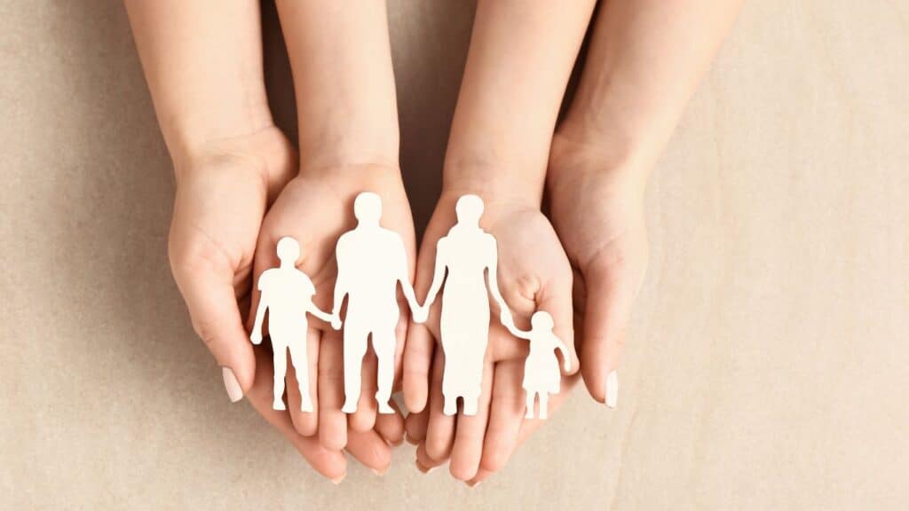 Hands of a woman and child with a family figure on a light background, symbolizing adoption.