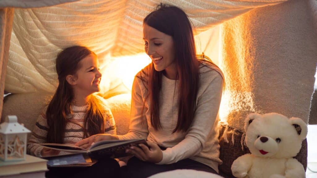 A mother and daughter enjoying storytime together inside a cozy sheet tent.