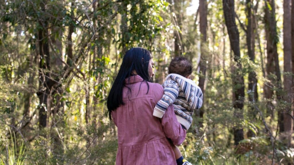 Mother carrying her baby in a sunlit forest.