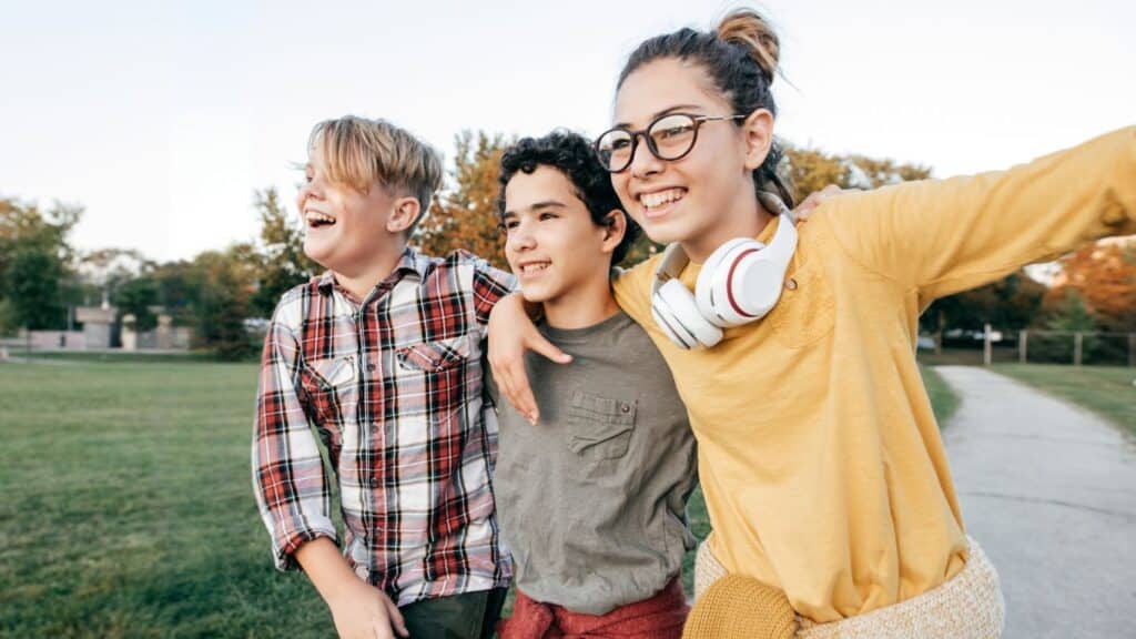 Three teens smiling and walking together outdoors.