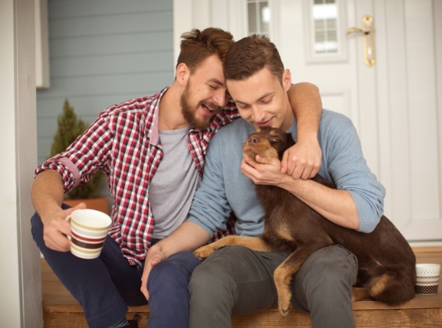 A same-sex couple sitting on a front porch with their dog.