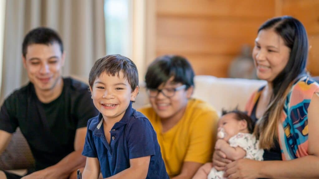A smiling family gathered in their living room, with a young boy in front and parents and siblings in the background.
